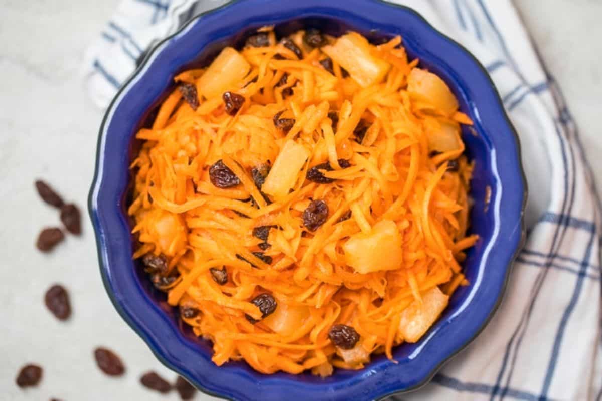 Easy Easter Recipes Shredded carrots tossed with raisins, pineapple, and a sweet dressing in a blue bowl.