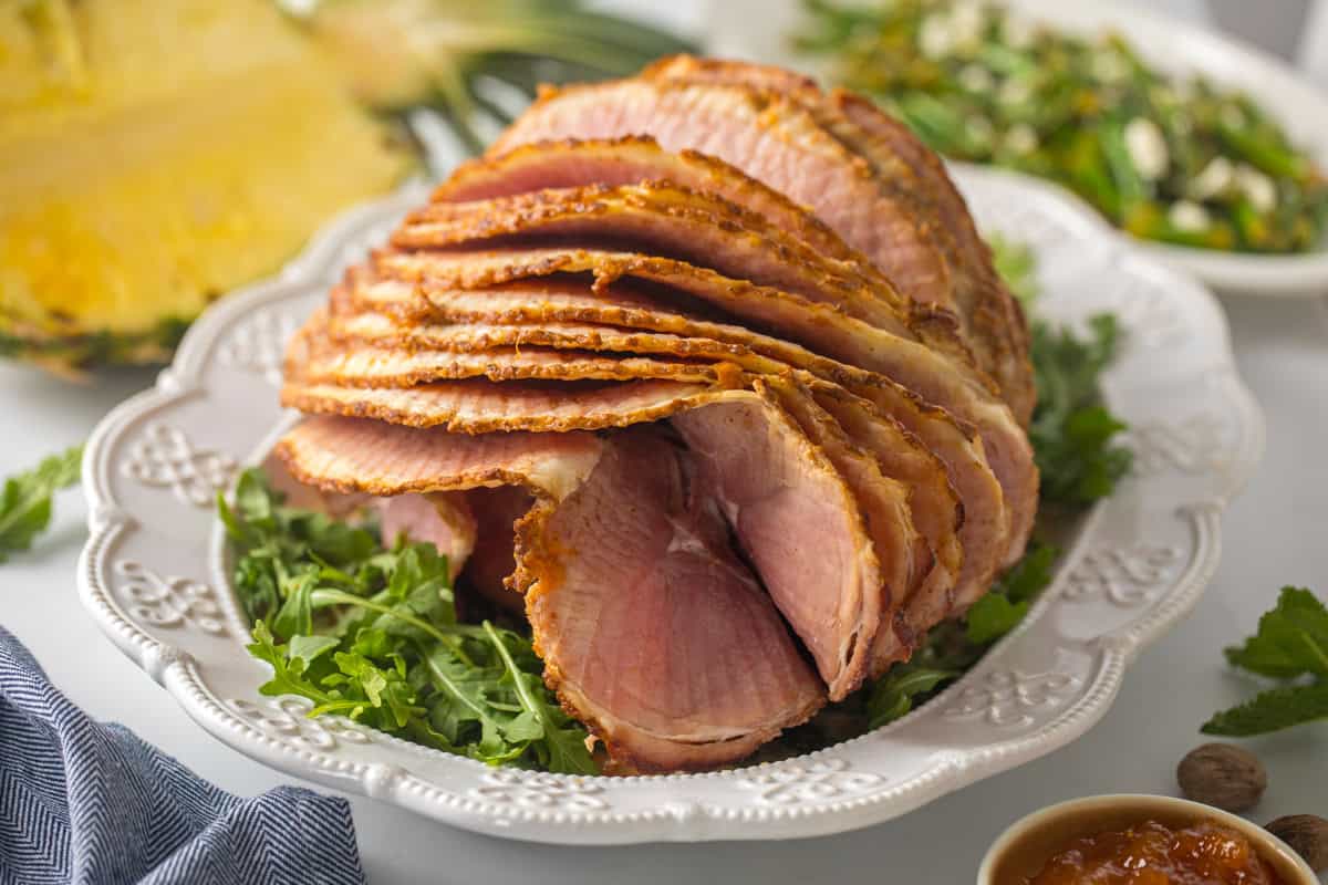 Easy Easter Dinner Recipes Spiral sliced glazed ham on white platter after baked and glazed with pineapple apricot glaze.