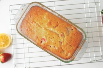 Baked strawberry loaf in pan on baking rack with holes poked in top for glaze to soak into bread.
