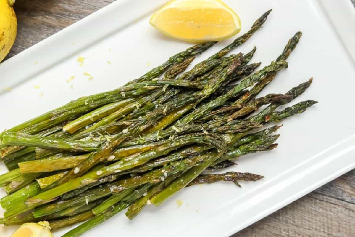 Simple Easter Dinner Menu Roasted Asparagus on white platter next to lemons topped with fresh parmesan.