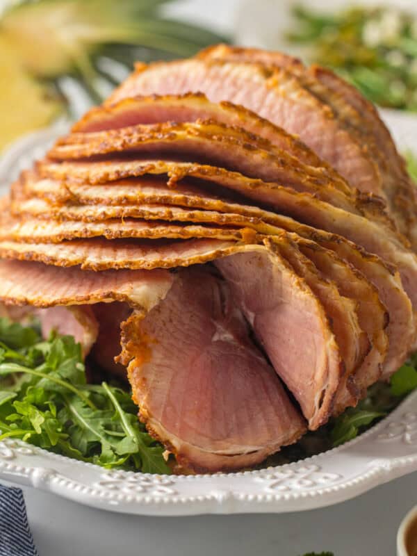 Spiral sliced ham on platter with pineapple glaze with fresh pineapple and asparagus salad in background.