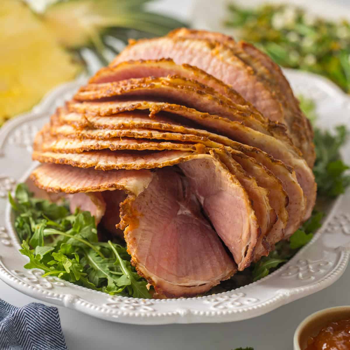 Holiday Dinner Ideas Spiral sliced ham on platter with pineapple glaze with fresh pineapple and asparagus salad in background.