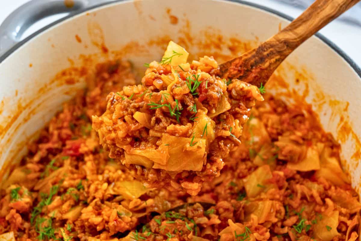 One Pot Unstuffed Cabbage Rolls Spoonful of cooked unstuffed cabbage rolls coming out of dutch oven topped with fresh dill.