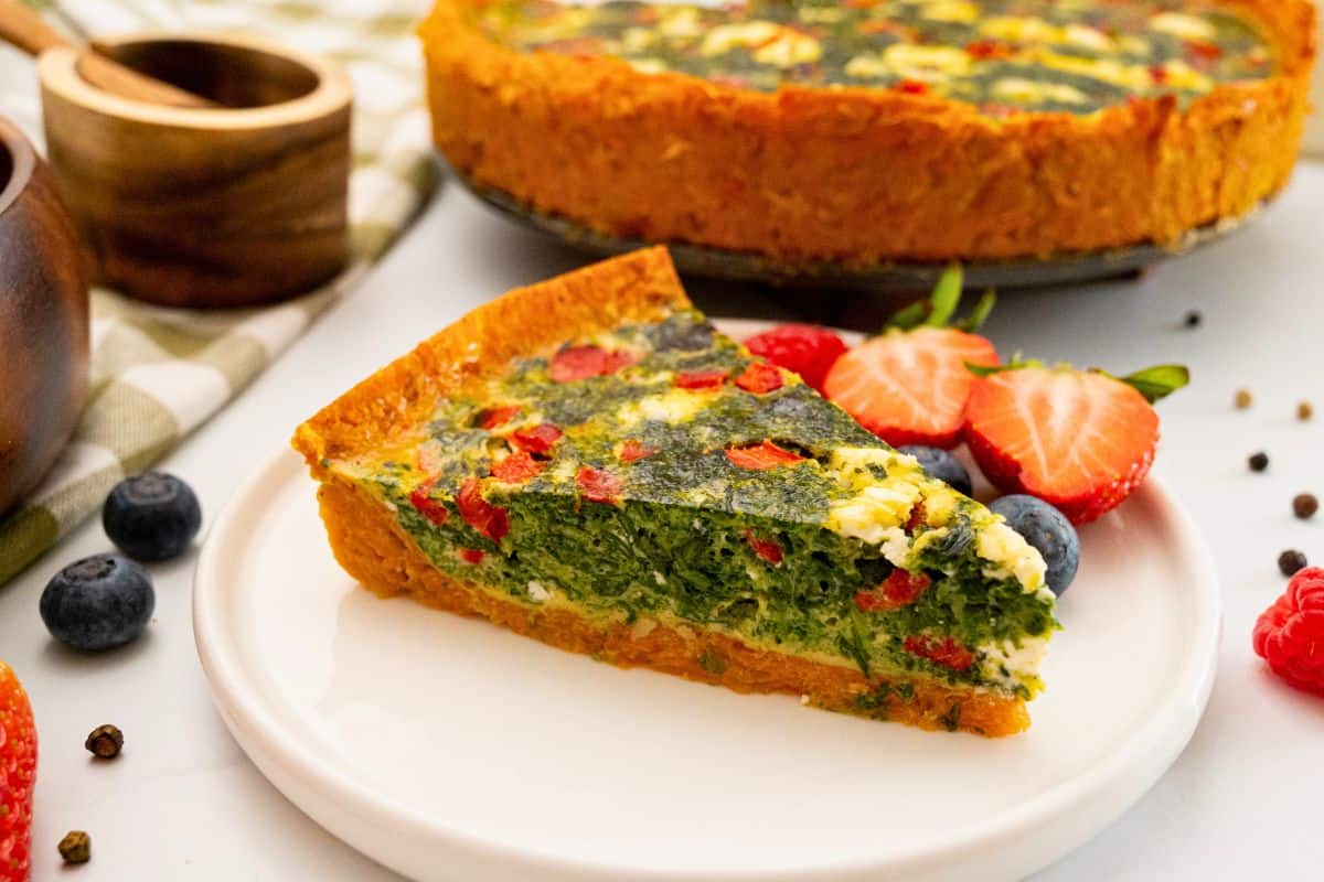 Gluten Free Easter Brunch Recipes Slice of Sweet Potato Quiche with spinach feta filling on White Plate served with fresh fruit.