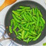 Crisp-tender bright green sugar snap peas in saute pan with melted butter and minced garlic.