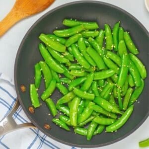 Crisp-tender bright green sugar snap peas in saute pan with melted butter and minced garlic.