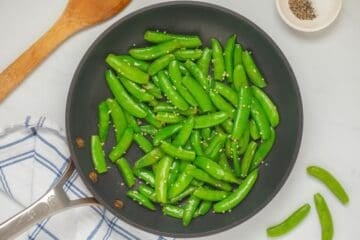 Bright green sugar snap peas in saute pan after being lightly steamed then sauteed with melted butter and minced garlic.