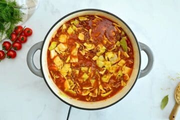 Large dutch oven with browned meat, beef stock, diced cabbage, tomatoes, and uncooked brown rice stirred together.