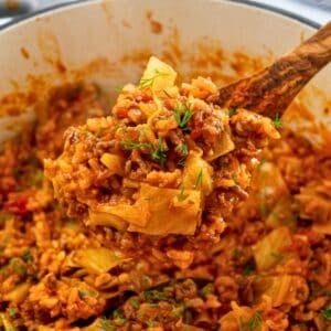 Spoonful of cooked unstuffed cabbage rolls coming out of dutch oven topped with fresh dill.