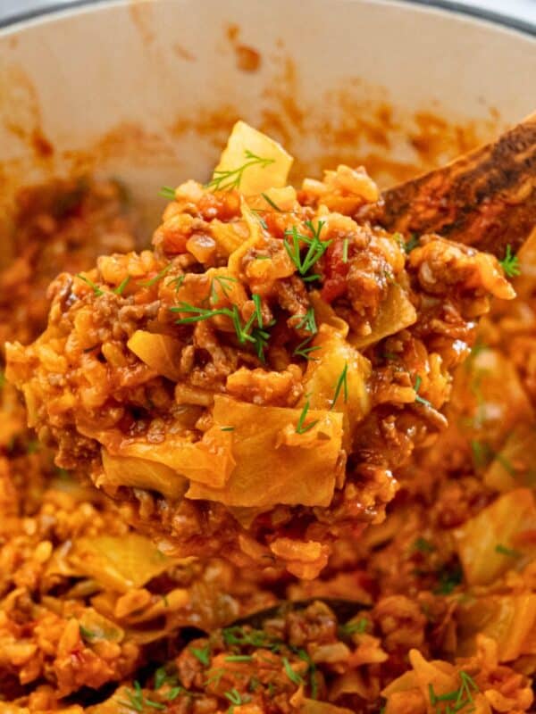 Spoonful of cooked unstuffed cabbage rolls coming out of dutch oven topped with fresh dill.