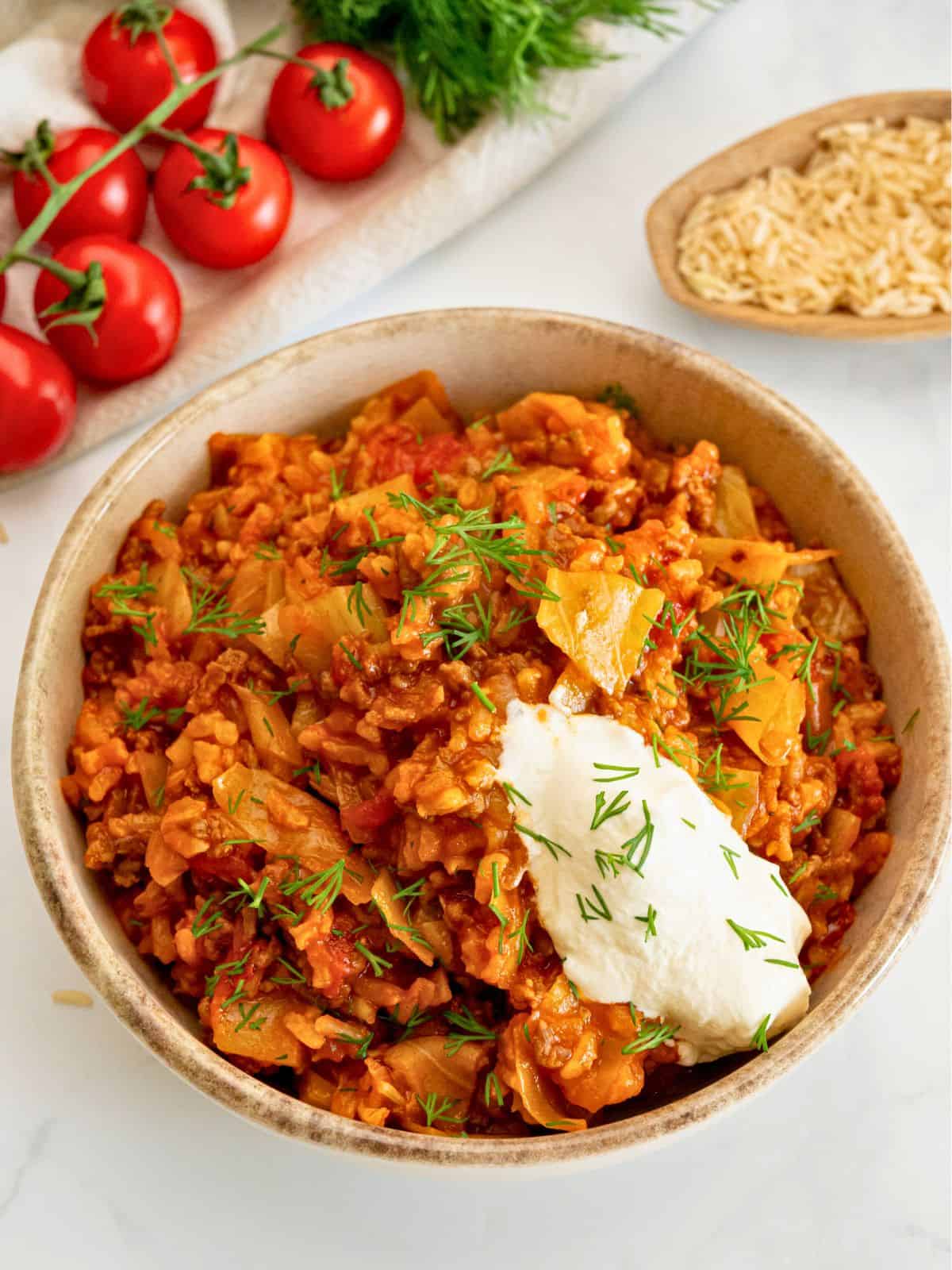 Unstuffed Cabbage Rolls Recipe Bowl of unstuffed cabbage rolls made with diced cabbage, ground beef, and brown rice topped with dollop of sour cream and fresh dill.
