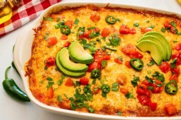 Baked Beef Enchilada Casserole in white casserole dish topped with sliced jalapeno, minced cilantro, and diced tomatoes.