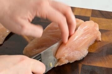 Thinly slicing chicken breasts into ½-inch strips against the grain for sheet pan chicken fajitas.