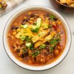 Bowl of Crockpot Chicken Tortilla Soup topped with diced avocado, homemade tortilla strips, shredded cheese and minced cilantro.