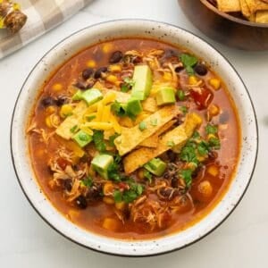 Bowl of Crockpot Chicken Tortilla Soup topped with diced avocado, homemade tortilla strips, shredded cheese and minced cilantro.