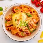 Bowl of cheesy baked pasta with creamy red sauce and sliced sausage topped with ribbons of basil.