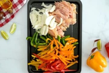 Sliced chicken breasts, bell peppers, sliced onions on rimmed sheet pan.