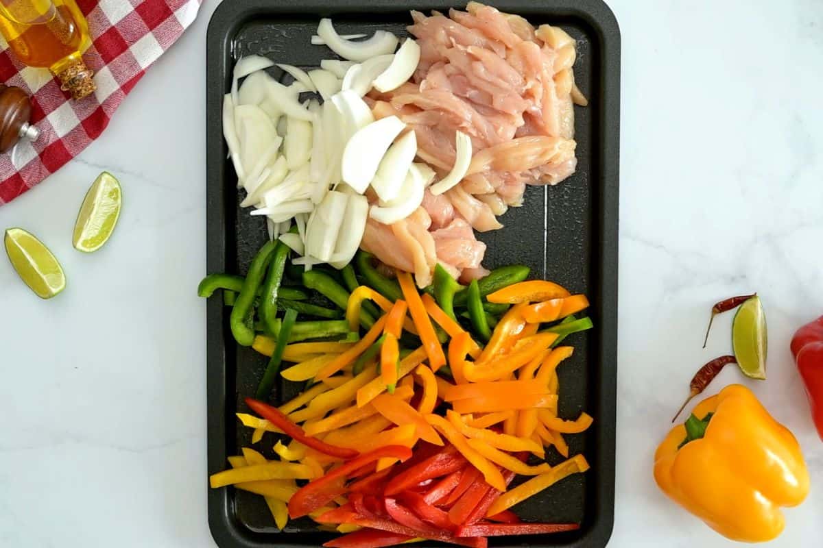 Chicken Fajitas Recipe with Onions and Peppers Sliced chicken breasts, bell peppers, sliced onions on rimmed sheet pan.