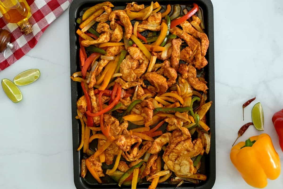 Oven Chicken Fajitas Sliced chicken breasts, sliced bell peppers, and sliced onions tossed with seasonings on rimmed sheet pan after baking.