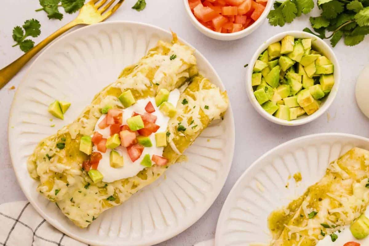 Dinner Recipes for Cinco De Mayo Salsa Verde Chicken Enchiladas on white plate topped with diced avocado and diced tomatoes.