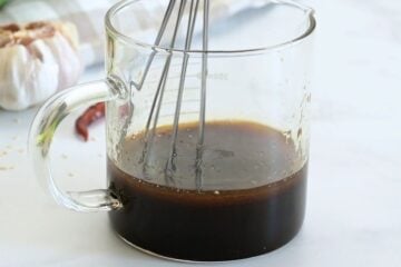 Soy sauce, rice vinegar, honey, sesame oil, and sriracha being whisked together in small glass measuring cup.