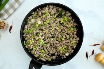 Browned ground turkey with green onions in skillet for base of egg roll in bowl.