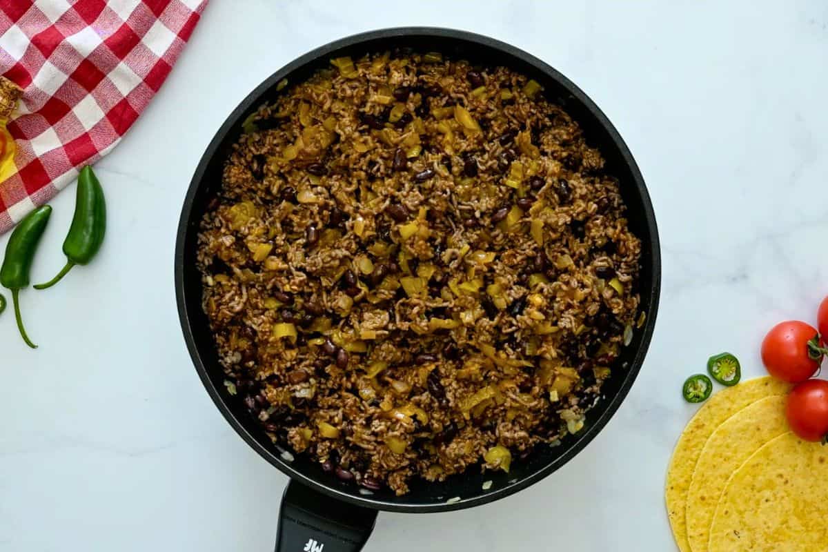 Layered Beef Enchilada Casserole Browned beef, onions, garlic, green chiles, and enchilada sauce in skillet for enchilada casserole filling.
