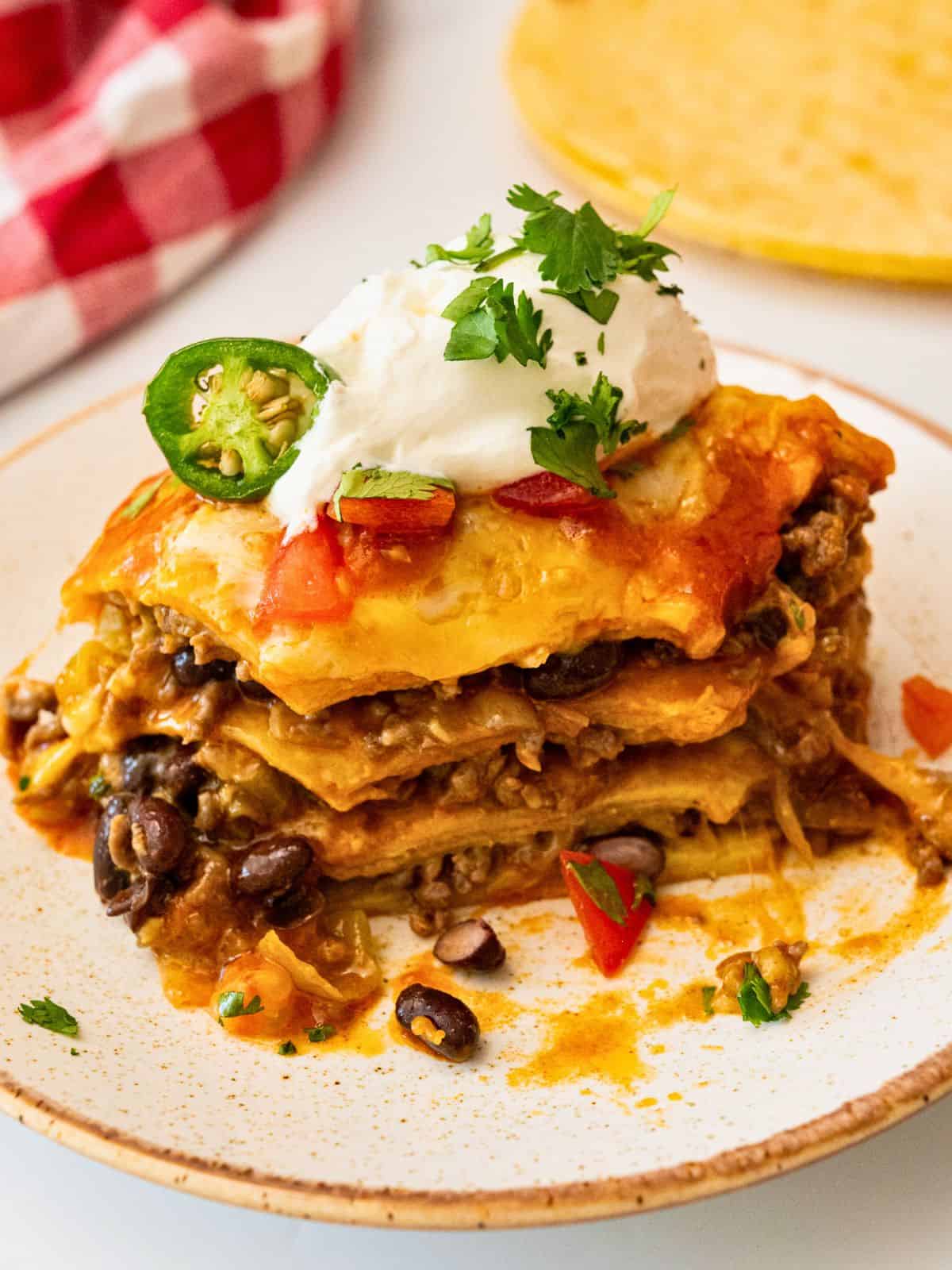 Enchilada Casserole Recipe with Ground Meat Beef Enchilada casserole on plate showing layers of seasoned ground beef, black beans, cheese, tortillas, and enchilada sauce.