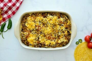 Layers of seasoned beef enchilada filling, corn tortillas, enchilada sauce, and cheese layered in 9x13-inch baking dish.