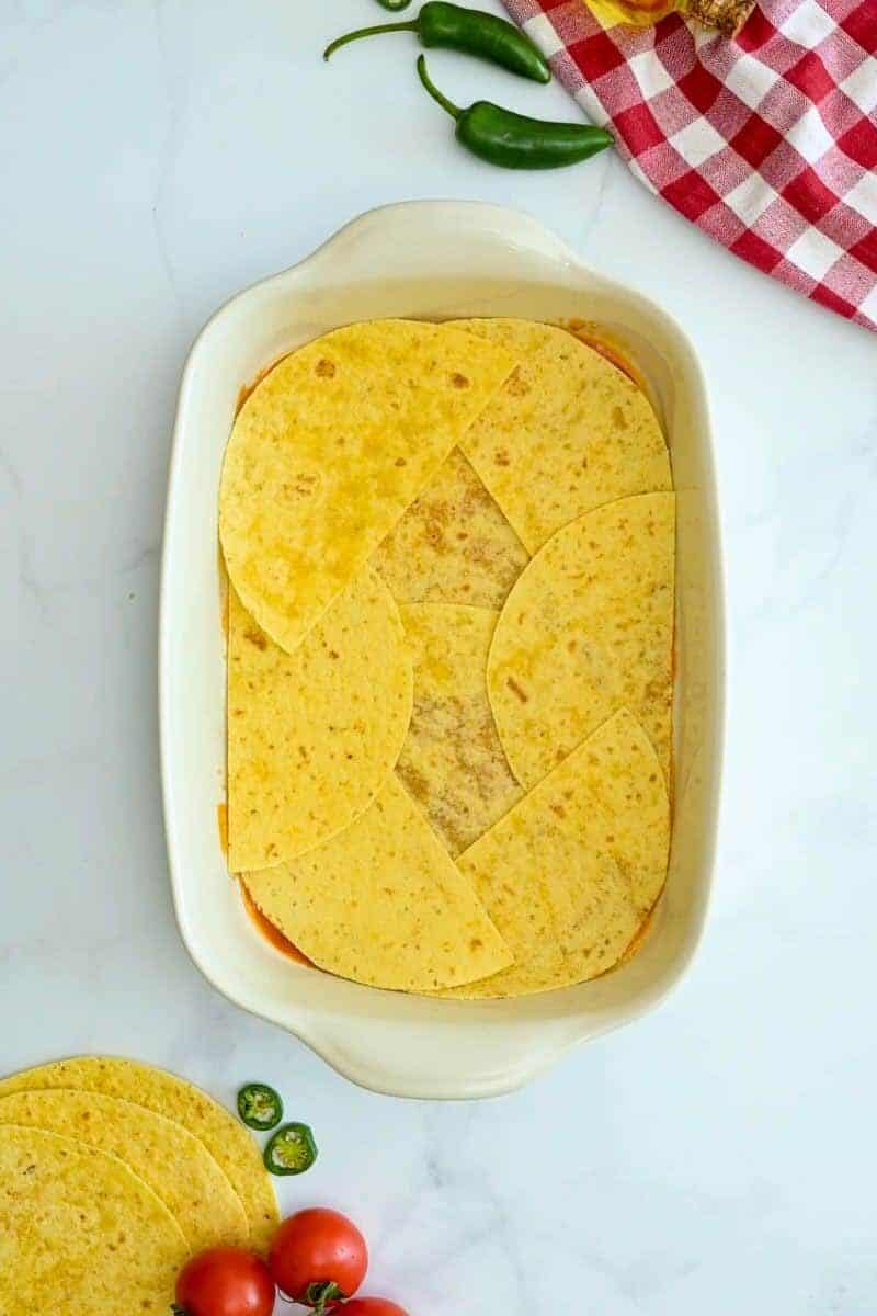 Easy Beef Enchilada Bake 9x13 inch baking dish lined with enchilada sauce and corn tortillas to fit for base of enchilada casserole.