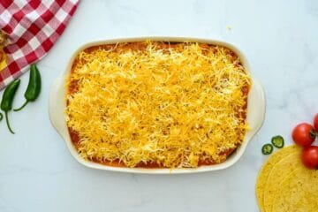 Layers of seasoned beef enchilada filling, corn tortillas, enchilada sauce, and cheese layered in 9x13-inch baking dish.