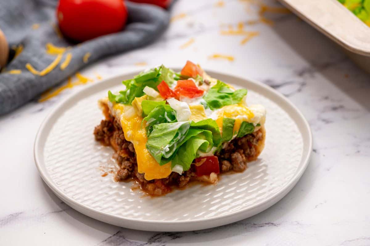 Cinco De Mayo Ideas that Keep it Simple Slice of Mexican Lasagna made with taco meat, flour tortillas, and a cottage cheese creamy layer topped with diced tomatoes and lettuce.