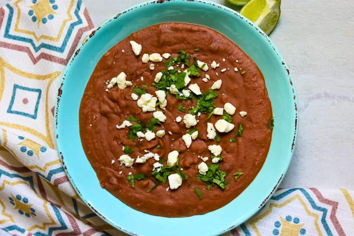 Ideas for Cinco de Mayo Menu Creamy blended Instant Pot refried beans in blue bowl topped with queso fresco and cilantro.