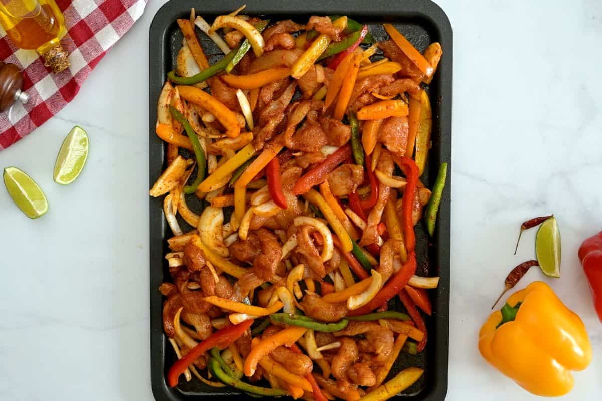 Oven Roasted Chicken Fajita Recipe Sliced chicken breast, raw bell peppers, and yellow onion on sheet pan tossed with fajita seasoning.