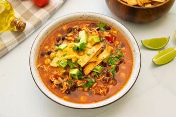 Bowl of Chicken Tortilla Soup topped with diced avocado, homemade tortilla strips, shredded cheese and minced cilantro.