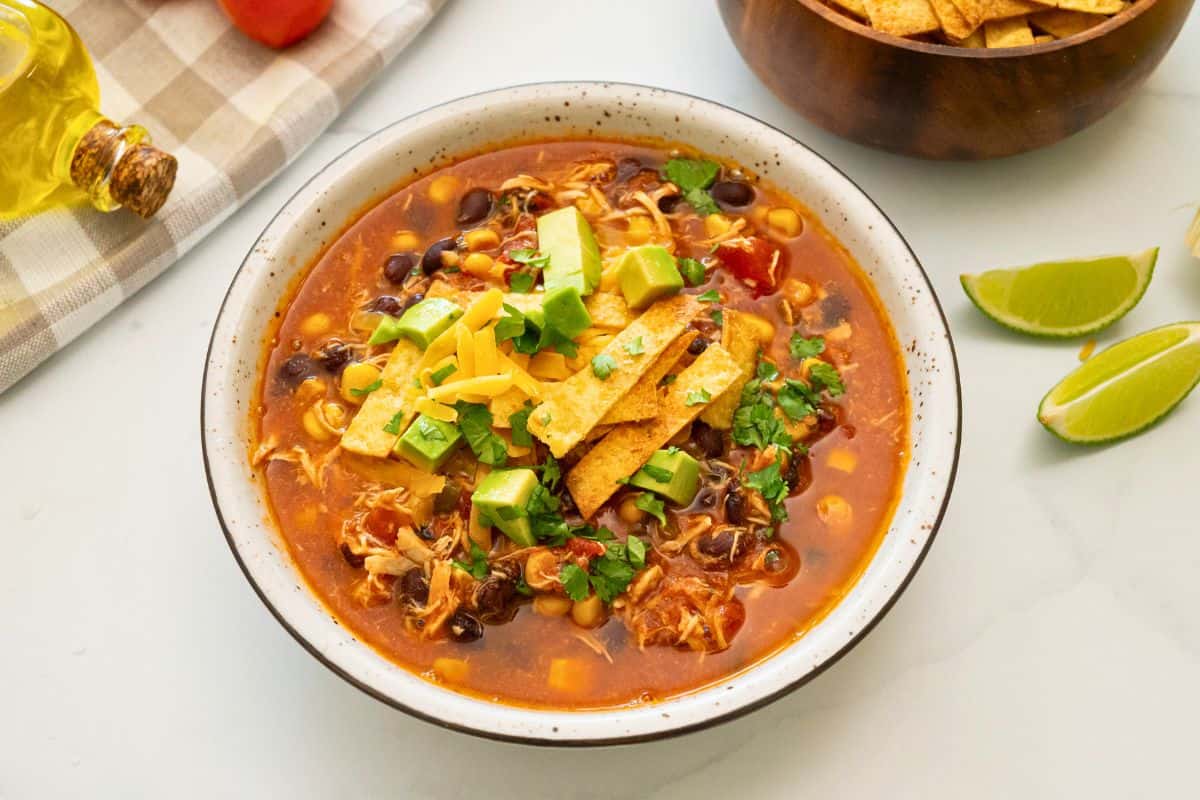 Slow Cooker Chicken Tortilla Soup Bowl of Chicken Tortilla Soup topped with diced avocado, homemade tortilla strips, shredded cheese and minced cilantro.