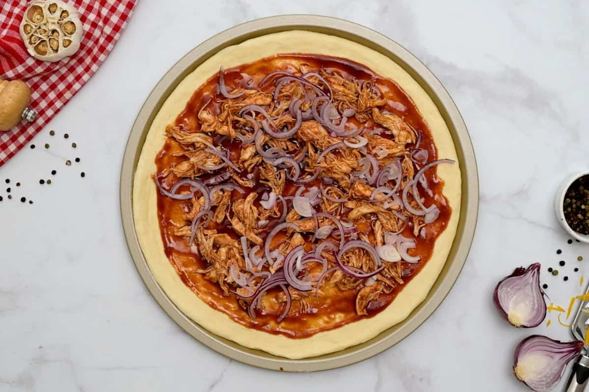 Easy BBQ Chicken pizza Pizza dough topped with thin layer of BBQ sauce, shredded BBQ chicken, red onions, and shredded cheese before baking.