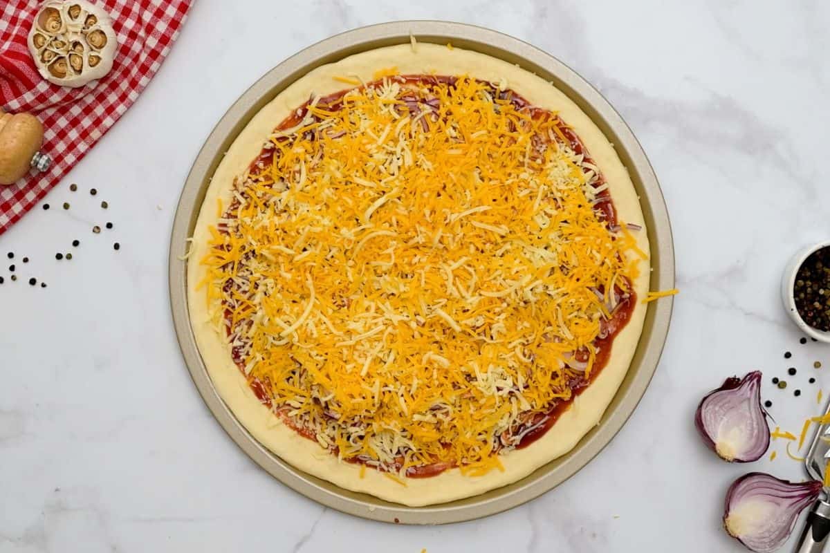 California Pizza Kitchen BBQ Chicken Pizza Pizza dough topped with BBQ sauce, shredded chicken, red onions, and shredded cheese before baking.