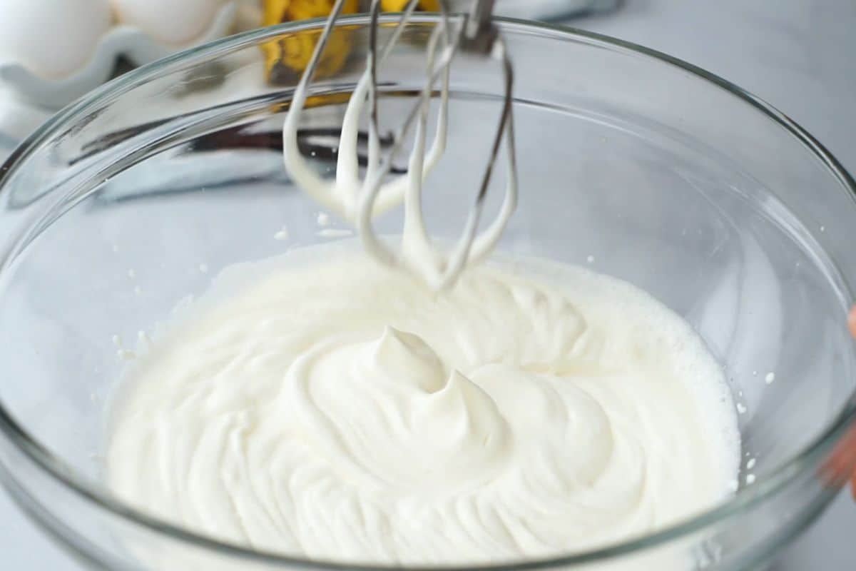 Metal beaters being lifted out of mixing bowl showing soft peaks in whipped cream.