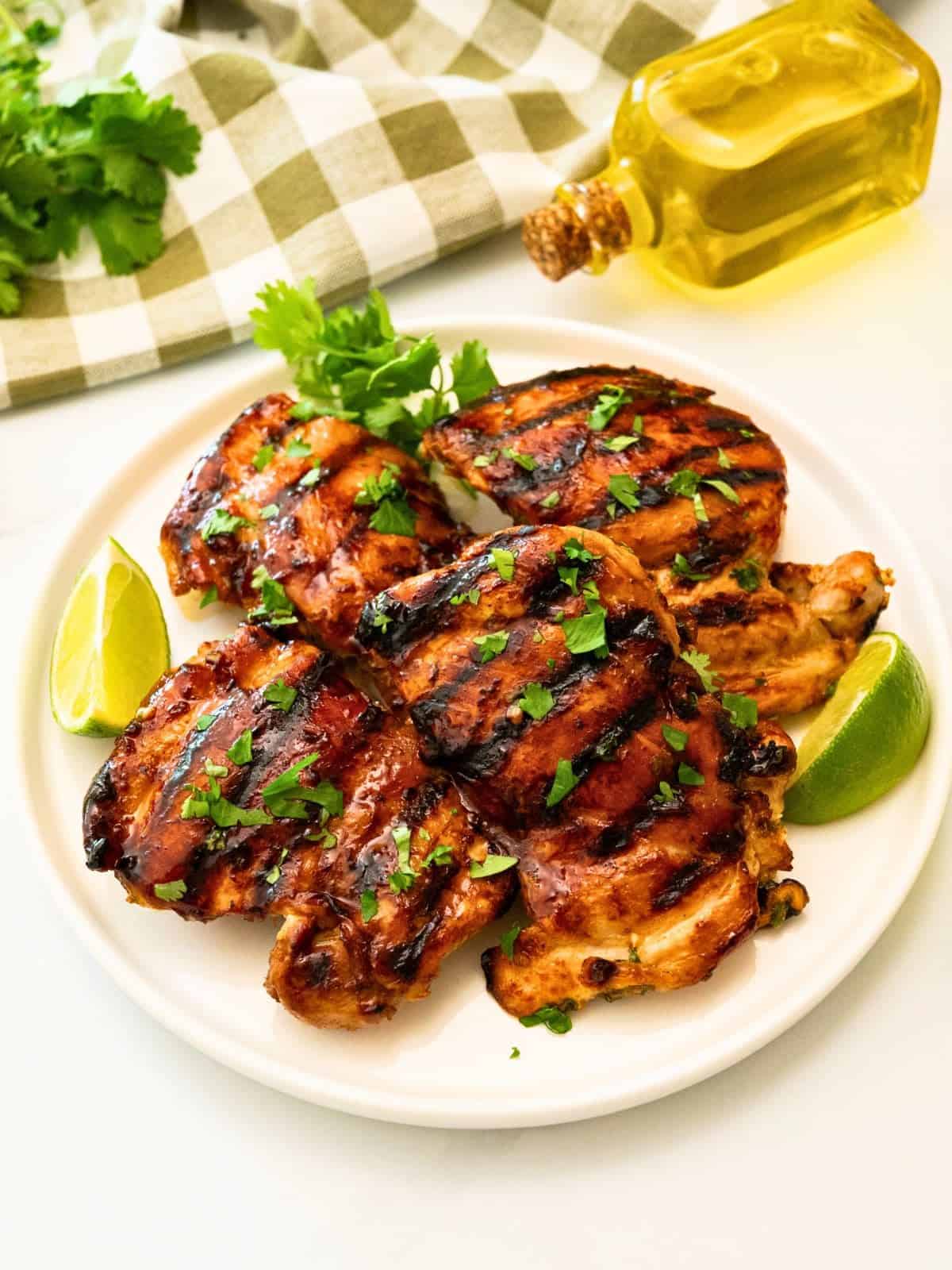 Cilantro Lime Chicken Marinade Grilled thighs that were marinated in cilantro lime marinade on platter topped with fresh cilantro next to fresh lime wedges.