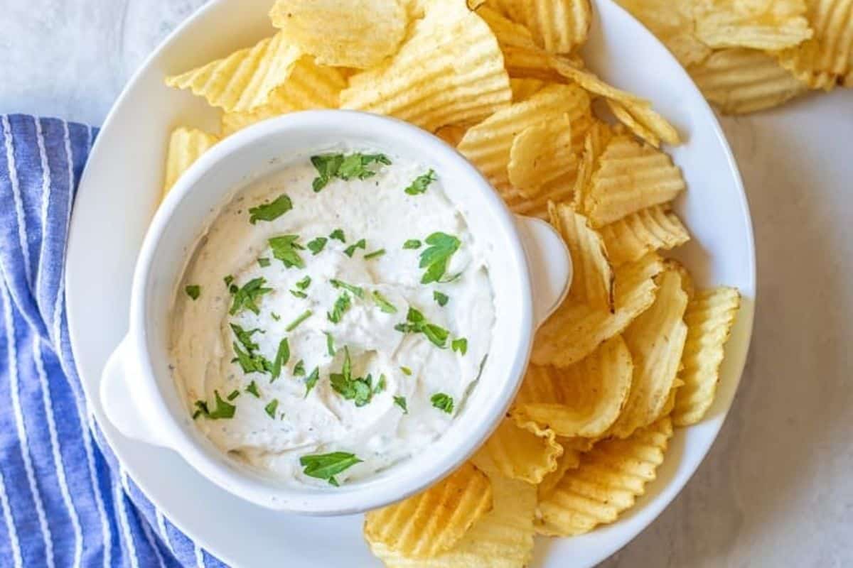 Bowl of chip dip made with dried seasonings and sour cream in bowl topped with fresh parsley served next to potato chips.