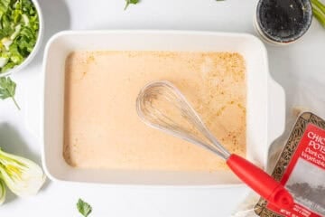 Canned coconut milk, soy sauce, sesame oil, curry paste, and rice vinegar in 9x13 inch baking dish with red whisk next to bag of frozen chicken and pork potstickers.