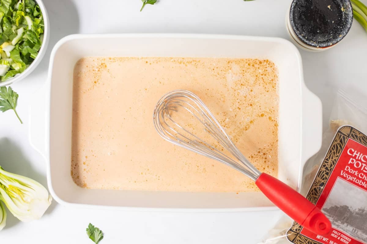 Canned coconut milk, soy sauce, sesame oil, curry paste, and rice vinegar in 9x13 inch baking dish with red whisk next to bag of frozen chicken and pork potstickers.