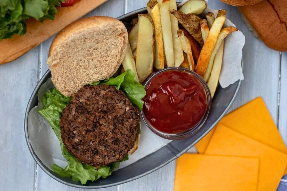 Homemade Black Bean Patty on Whole Wheat Bun next to lettuce, sliced cheese, and side of homemade fries.