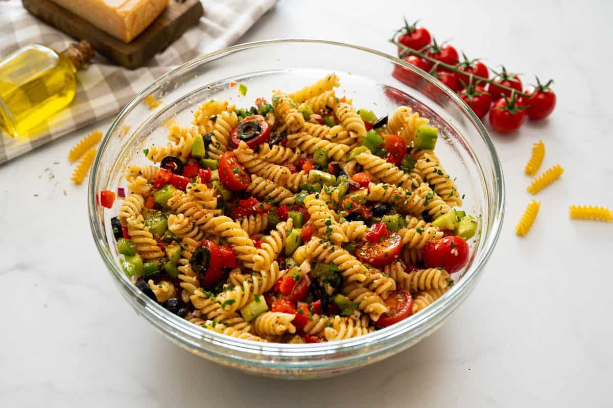 Mixing bowl with rotini noodles tossed with Italian dressing, peppers, cucumbers, olives, tomatoes, and salad supreme seasoning.