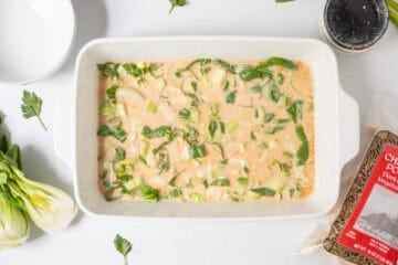 Sliced bok choy mixed into coconut milk, soy sauce, sesame oil, curry paste, and rice vinegar in 9x13 inch baking dish next to bag of frozen chicken and pork potstickers.