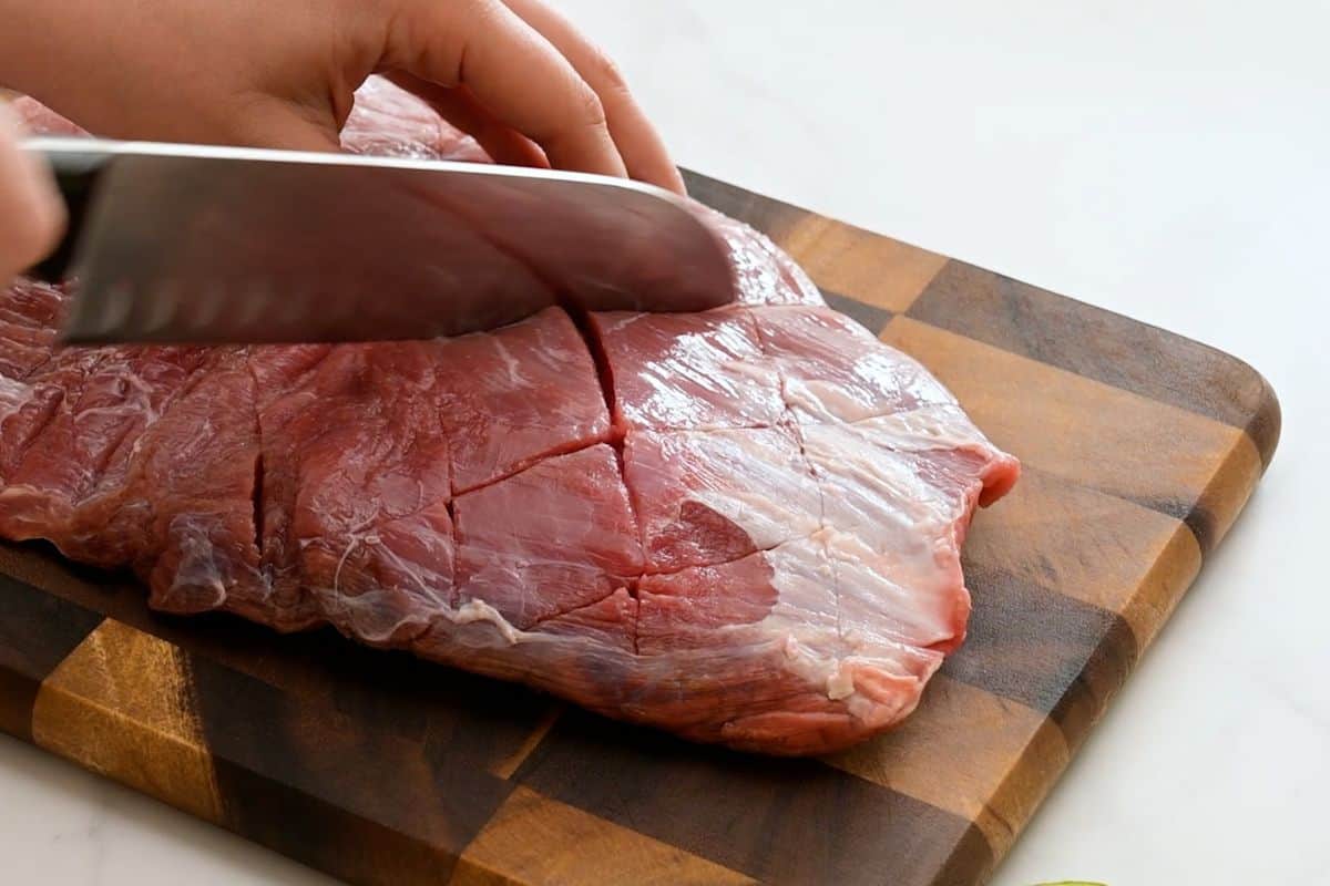 Grilled Marinated Flank Steak Chef's knife scoring flank steak with diagonal cuts before marinating.