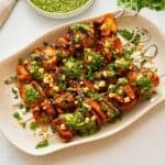 Grilled chicken kabobs on white platter topped with cilantro pesto, fresh cilantro, and chopped peanuts.