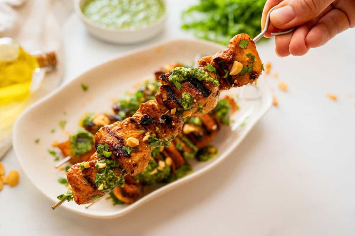Chicken Kabobs on Grill Close up of one grilled chicken kabobs topped with cilantro pesto, fresh cilantro, and chopped peanuts.
