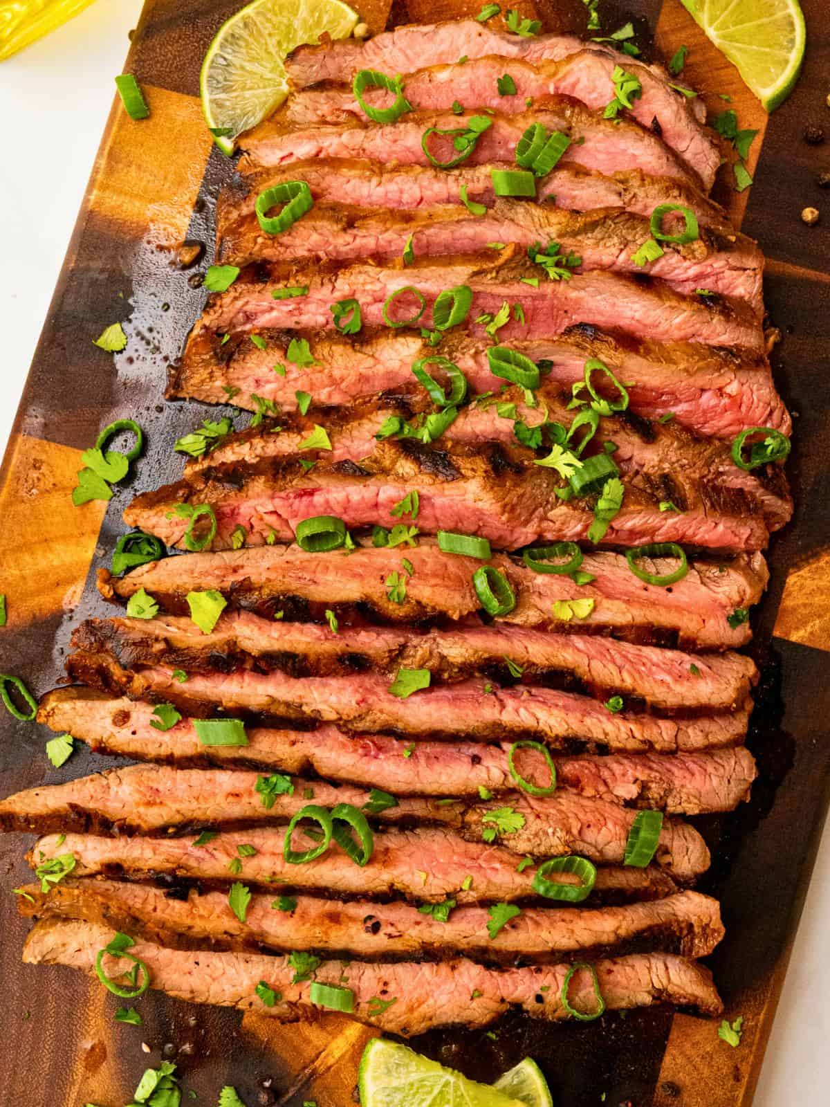 Marinated Flank Steak Marinated grilled flank steak sliced against the grain topped with cilantro, green onions, lime slices.